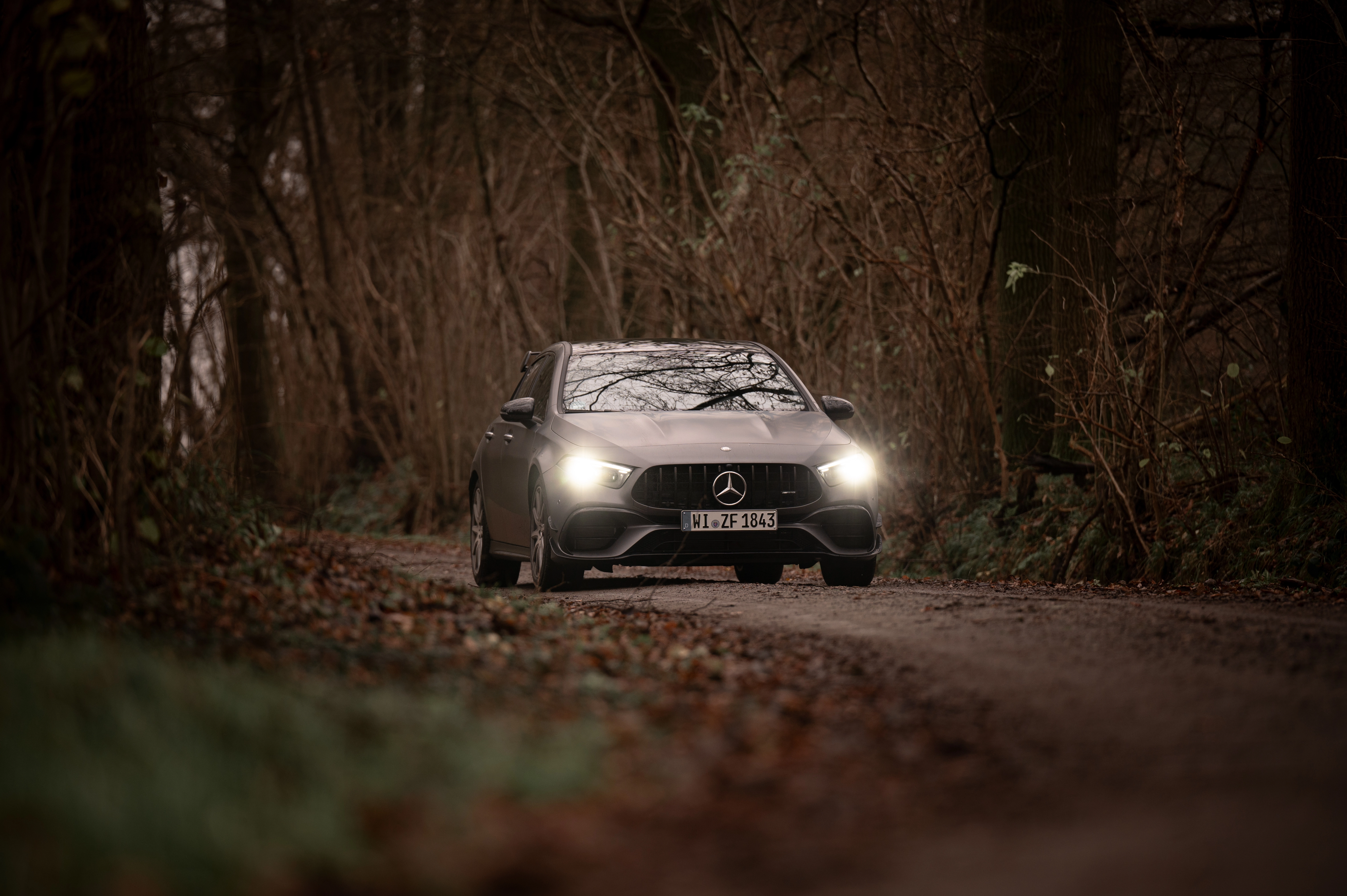Mercedes-AMG A 45 S von vorne auf Waldweg mit Scheinwerfern